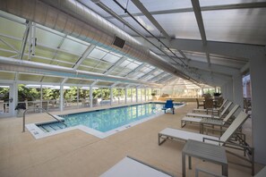 Una piscina interior con techo de cristal, sillas de descanso y una tumbona.