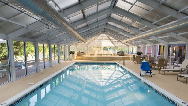 An indoor swimming pool with clear glass ceiling, tiled steps leading into the pool, and lounge chairs around the pool area.
