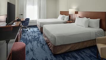 A hotel room with two beds, a desk with a TV, a chair, and a red ottoman.