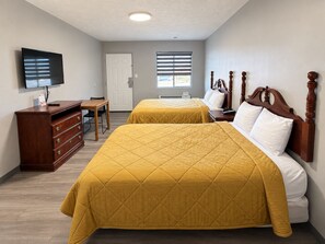 Habitación de hotel con dos camas, un televisor, un aparador de madera, un escritorio y una ventana con persianas.