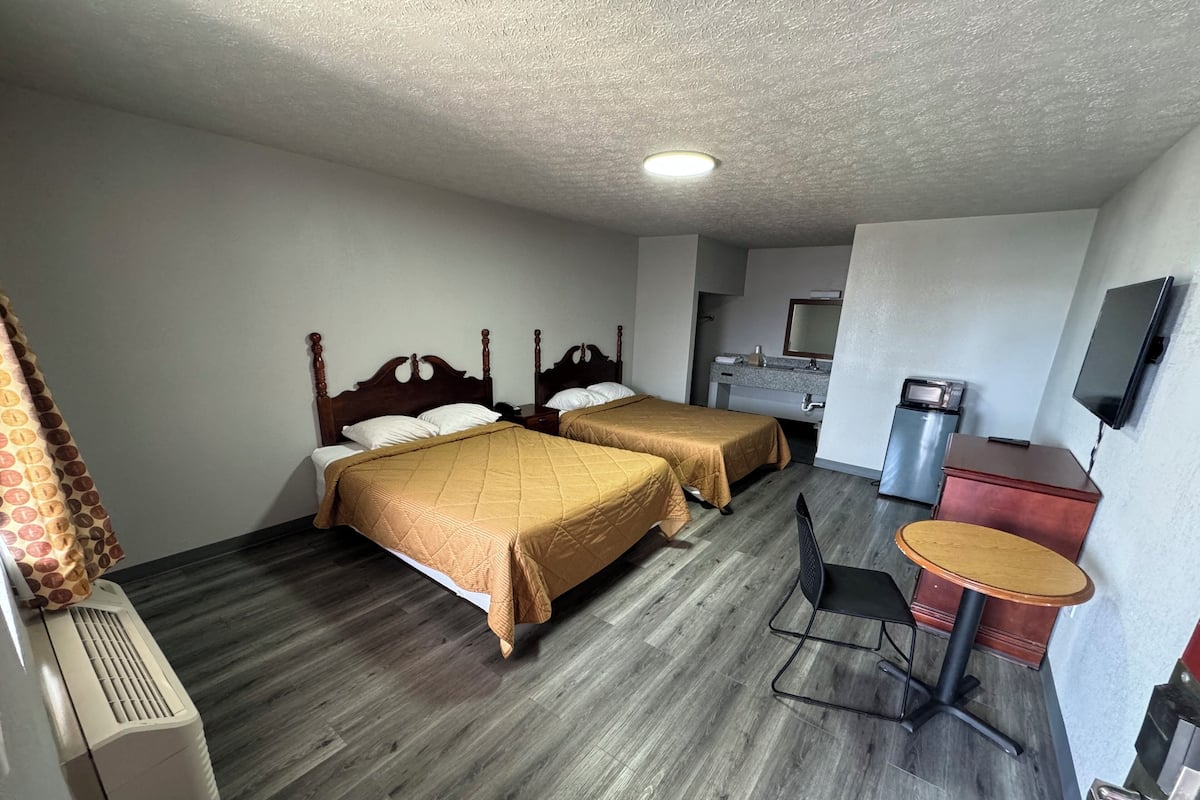 A hotel room with two beds, a desk, a chair, a television, and a kitchenette.