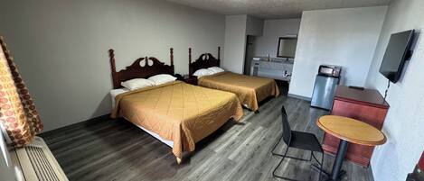 A hotel room with two beds, a desk, a chair, a television, and a kitchenette.