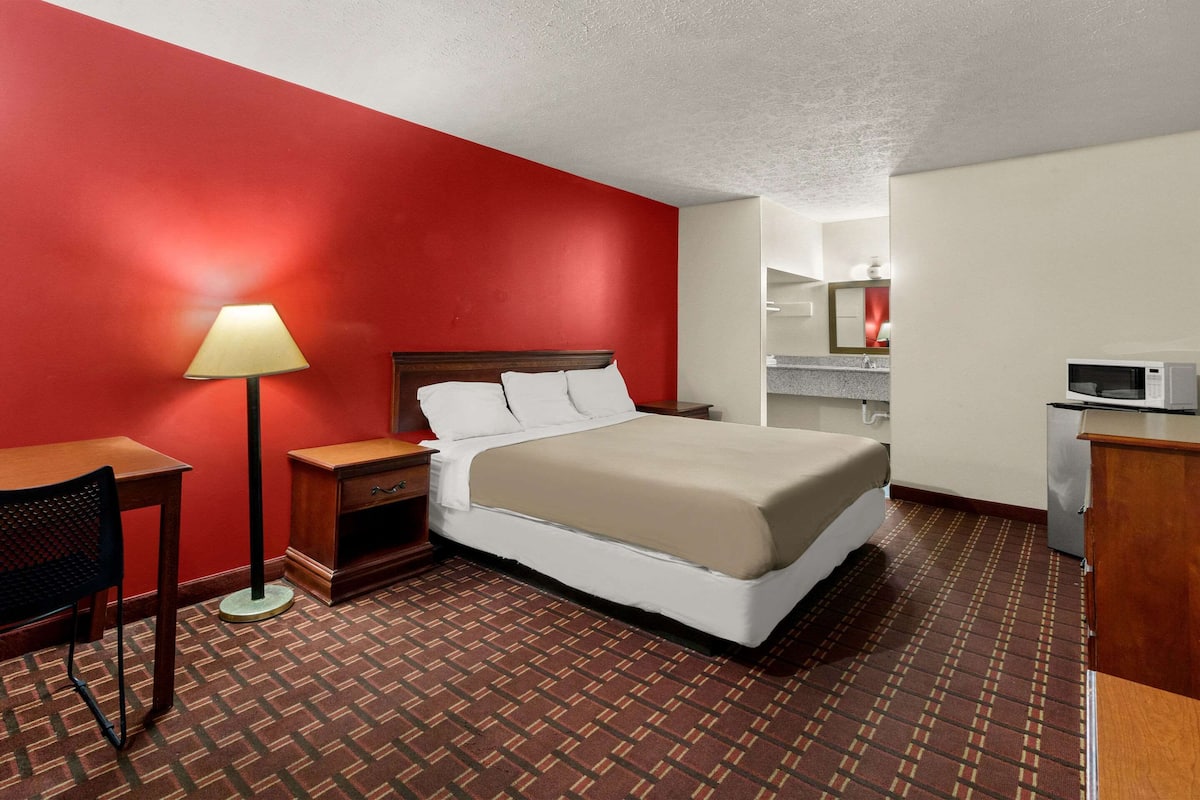 A hotel room with a large bed, a desk with a lamp, a microwave, and a small cabinet.
