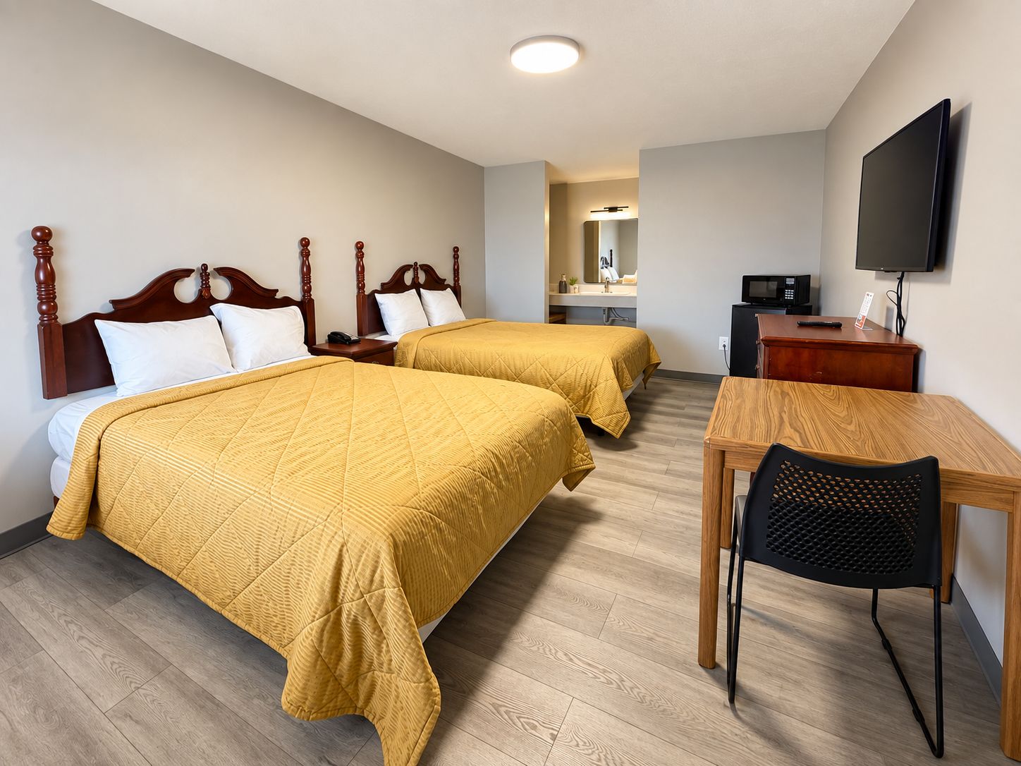 A hotel room with two beds, a desk, a chair, a television, and a mirror.