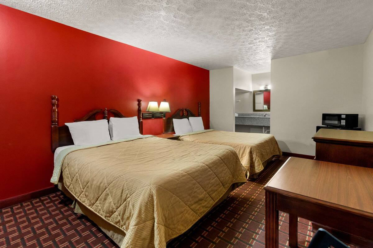 A hotel room with two beds, a desk, a chair, a TV, and a bathroom visible through an open door.