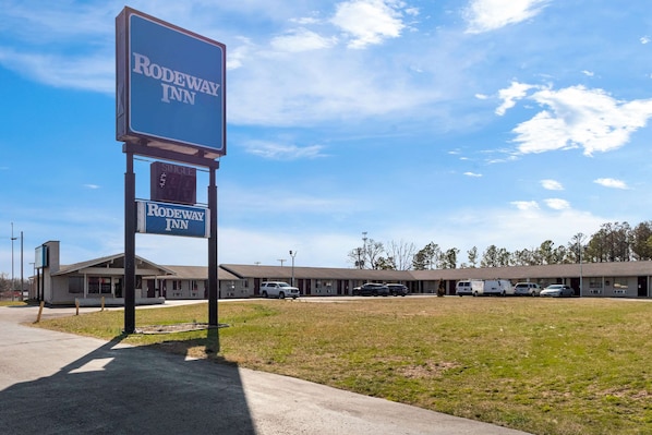 A motel named Rodeway Inn with a signboard, a parking lot, and a building with multiple rooms.