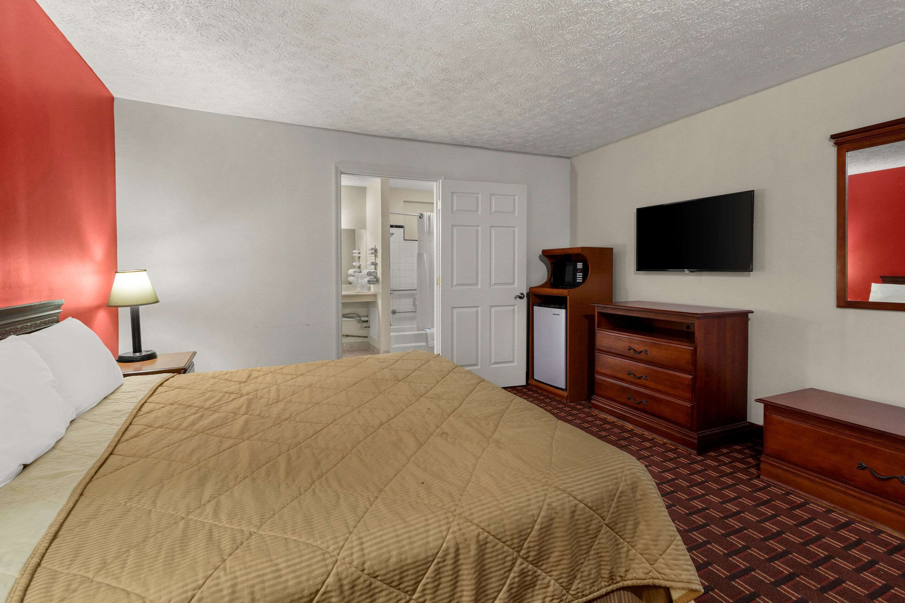 A hotel room with a bed, a television, a microwave, and a dresser.