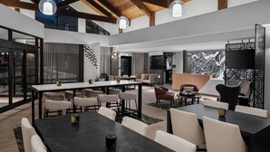 A spacious, modern interior with high ceilings and exposed beams, featuring multiple seating areas, a large dining table, and a large flat-screen TV. - AC Hotel by Marriott Park City (Park City)