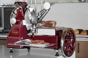 A vintage meat slicer with a plate of sliced meat and a loaf of bread.