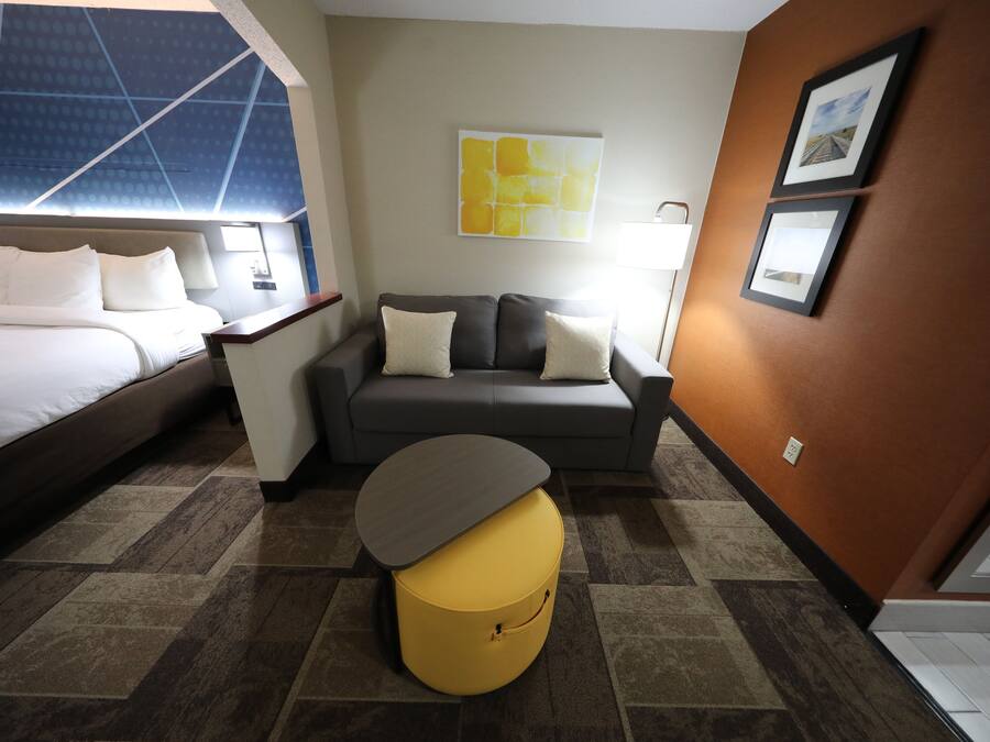 A hotel room with a bed, a sofa, a small table, and a yellow ottoman.