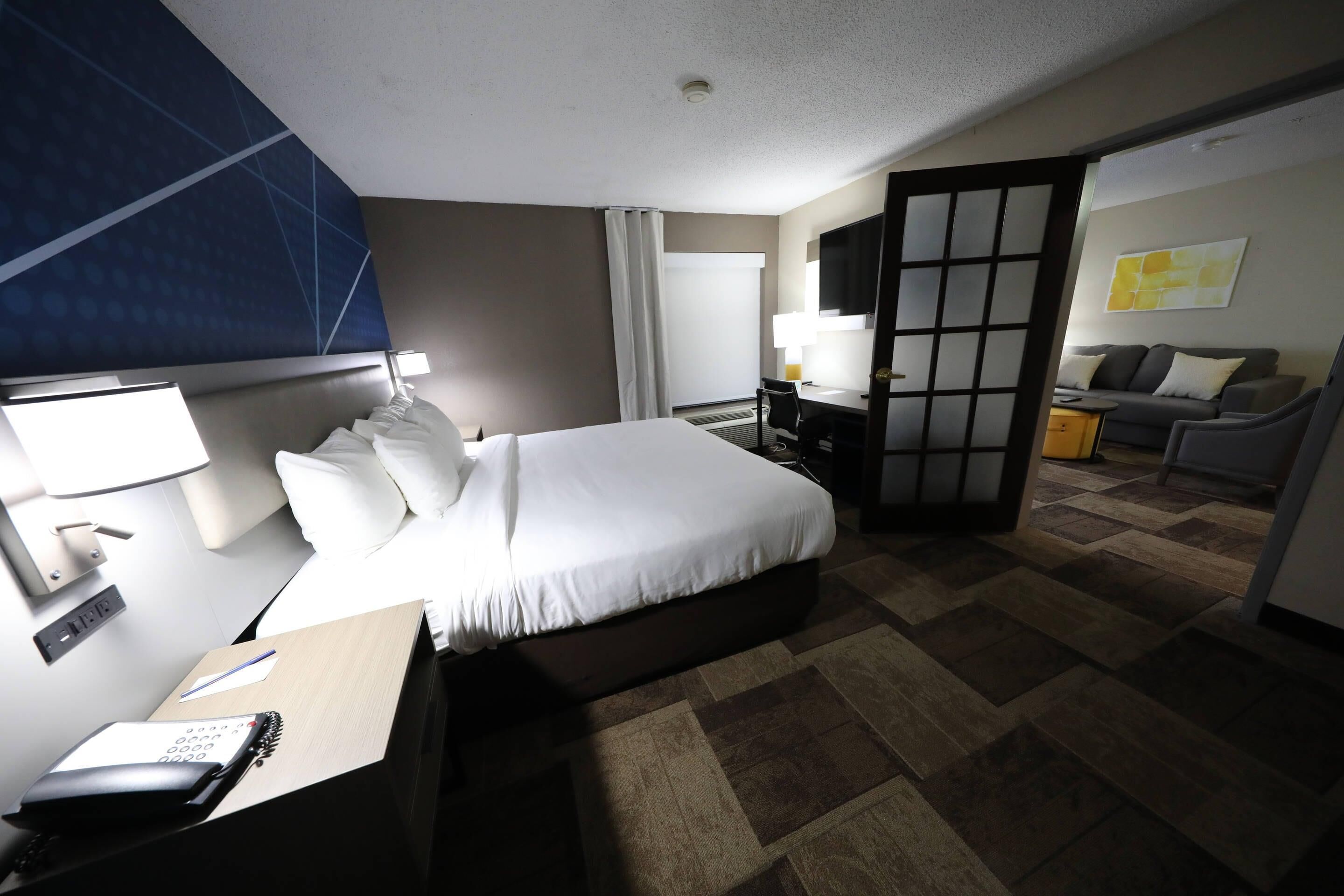 A hotel room with a bed, desk, chair, and a view of the outside.