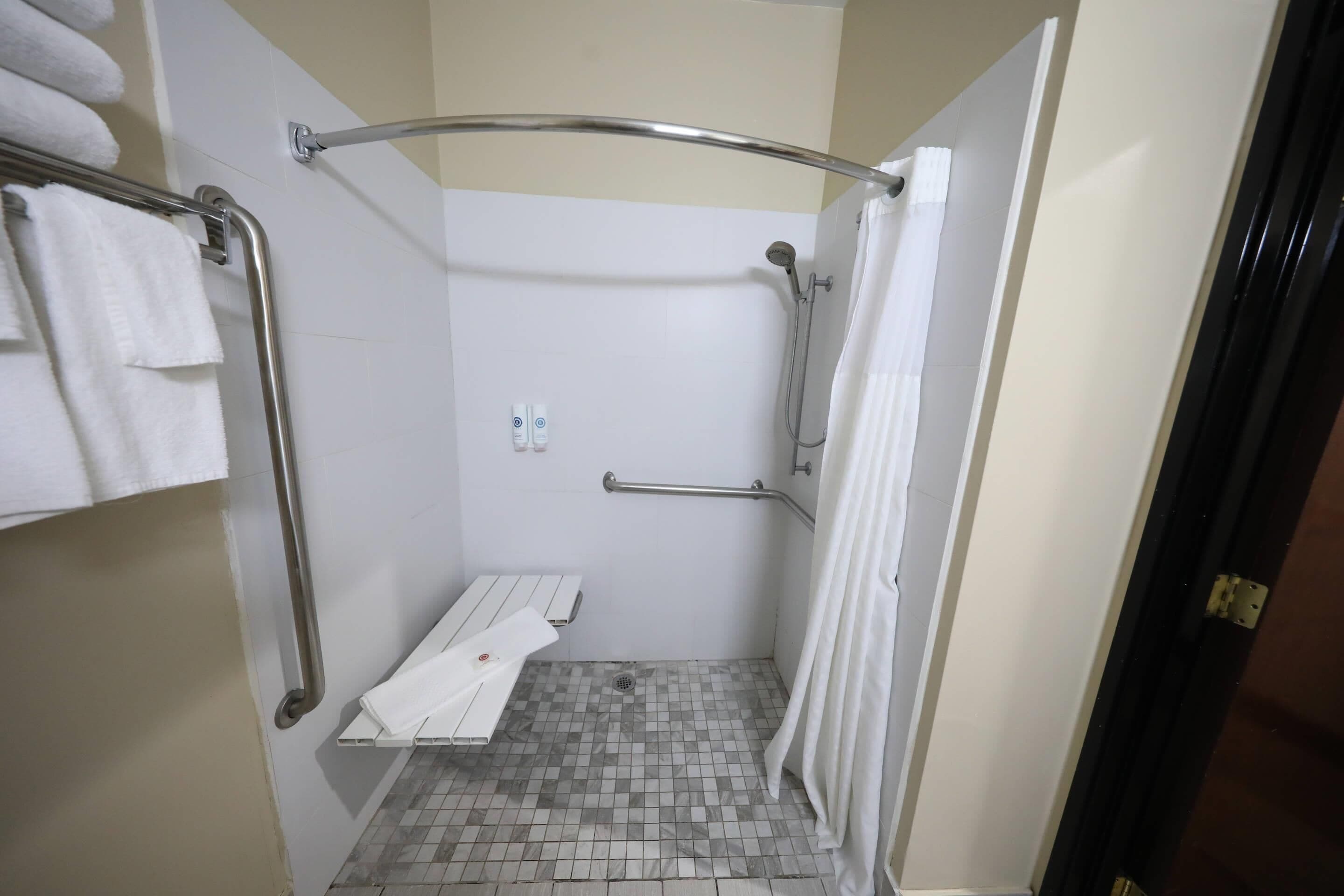 A shower with a grab bar, a white towel rack, and a shower curtain.