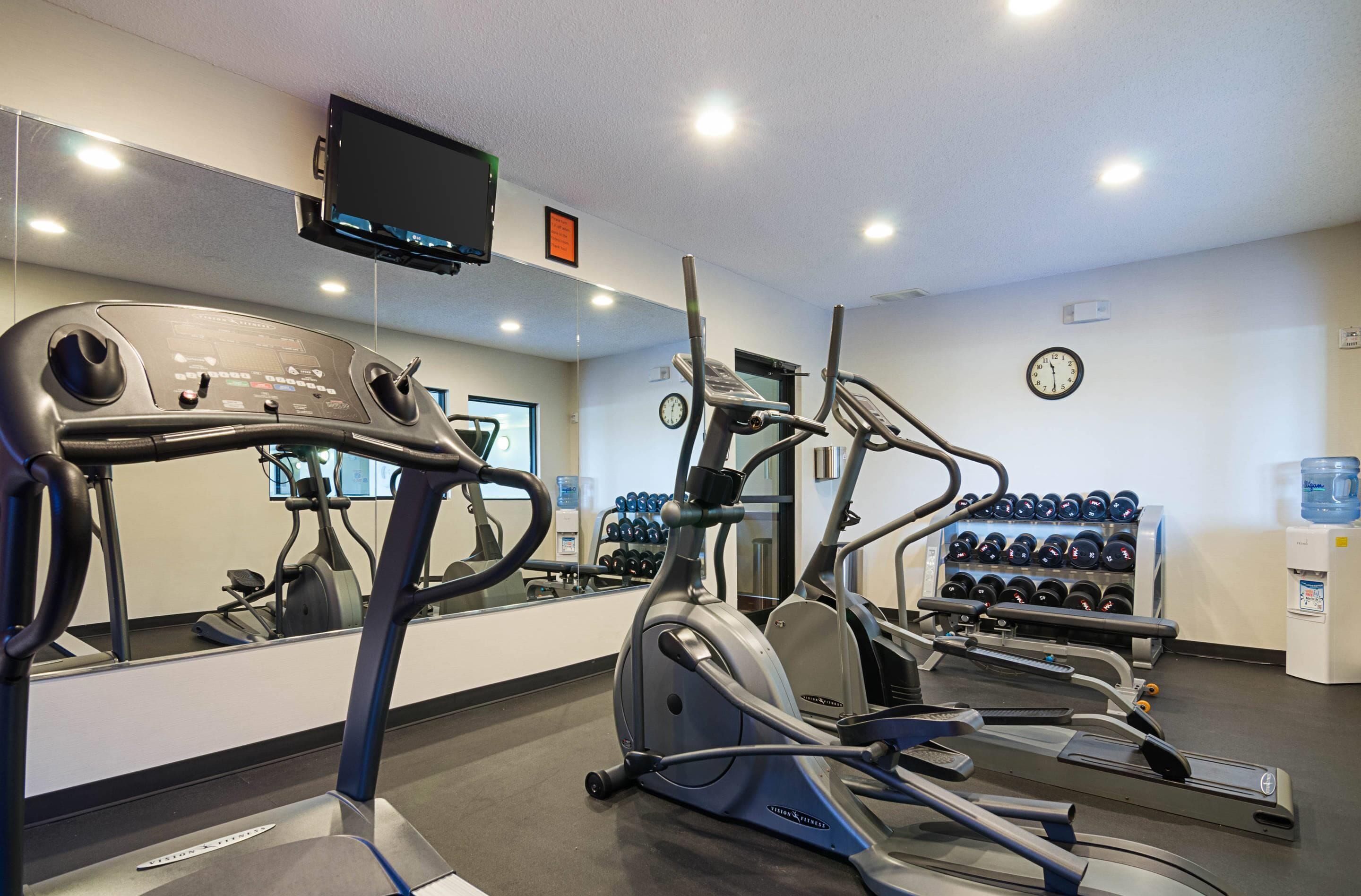 Une salle de sport équipée d’appareils de cardio, d’un téléviseur, d’une horloge et d’un distributeur d’eau.