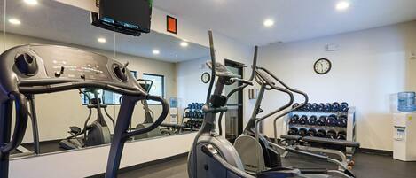 Une salle de sport équipée d’appareils de cardio, d’un téléviseur, d’une horloge et d’un distributeur d’eau.