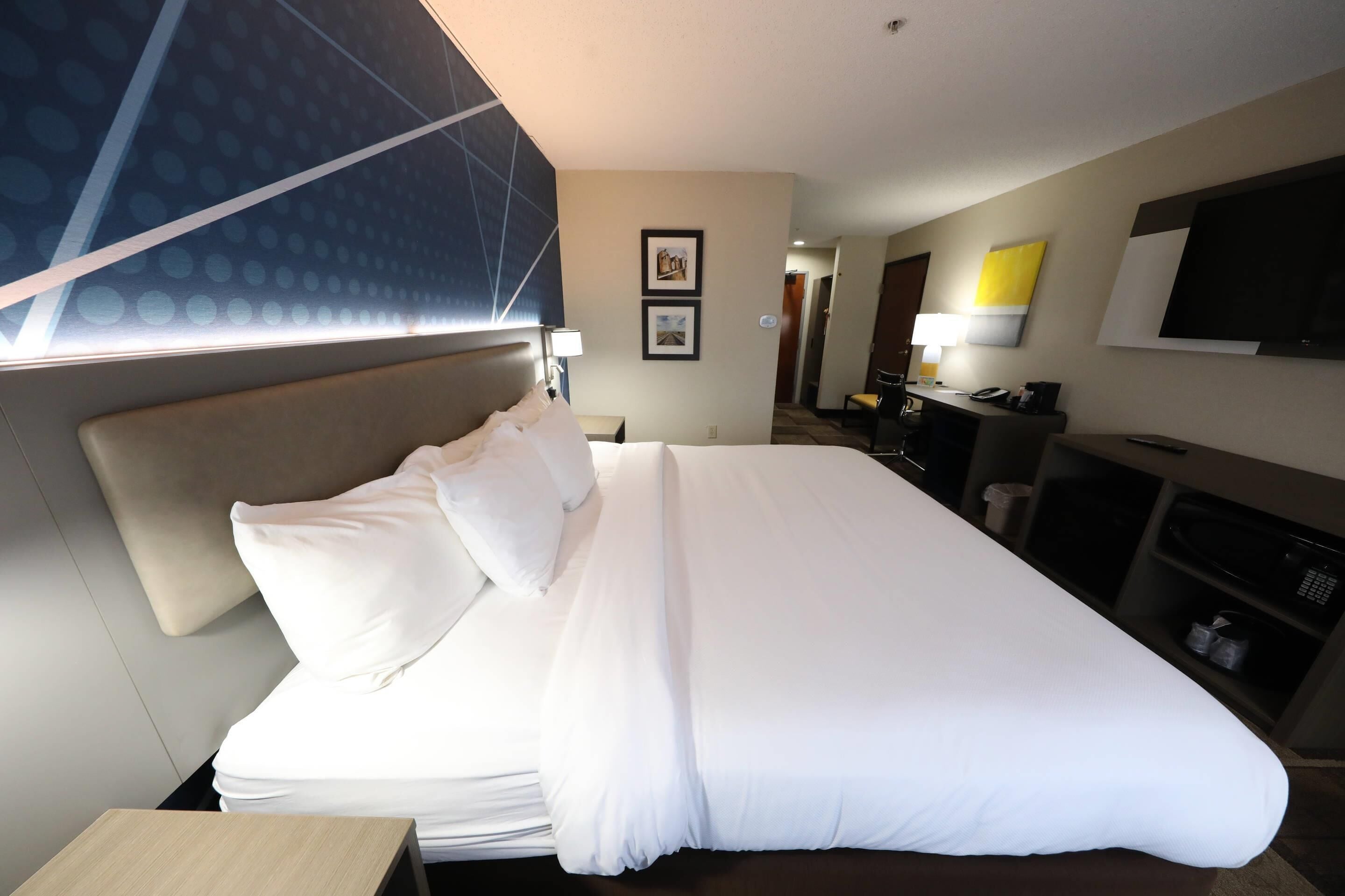 Ein Hotelzimmer mit einem großen Bett, einem Schreibtisch, einem Sessel, einem Fernseher und einem Wandregal.