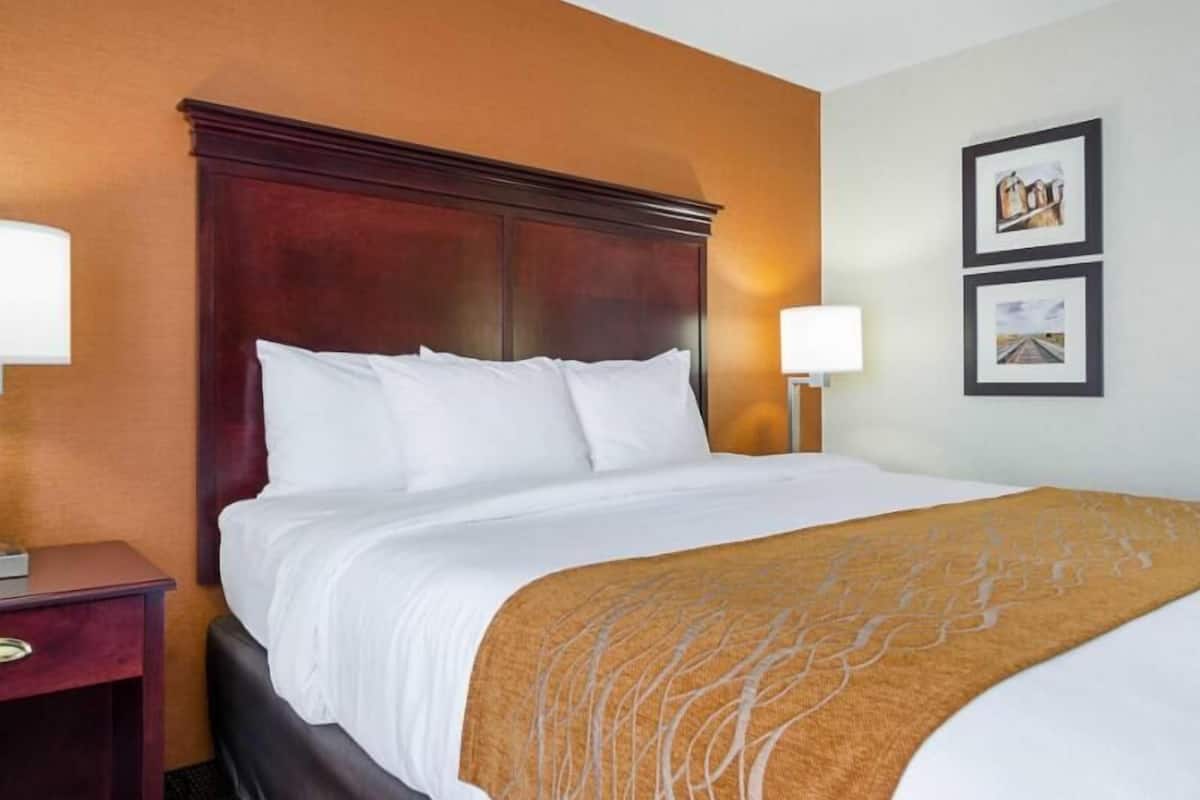 A hotel room with a large bed, wooden headboard, two bedside lamps, and framed pictures on the wall.