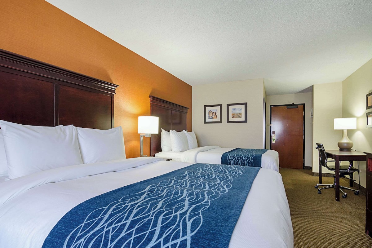 A hotel room with two beds, a desk, a chair, and a door.