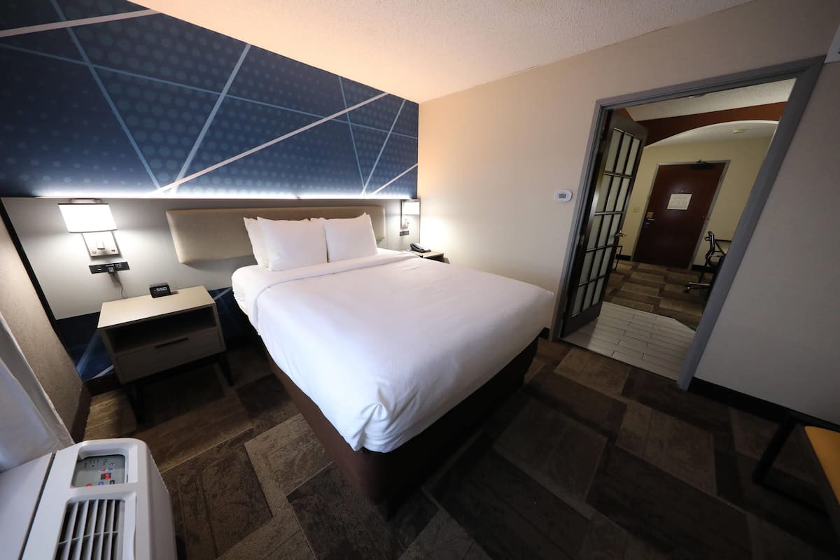 A hotel room with a bed, bedside tables, a heater, and a mirror.