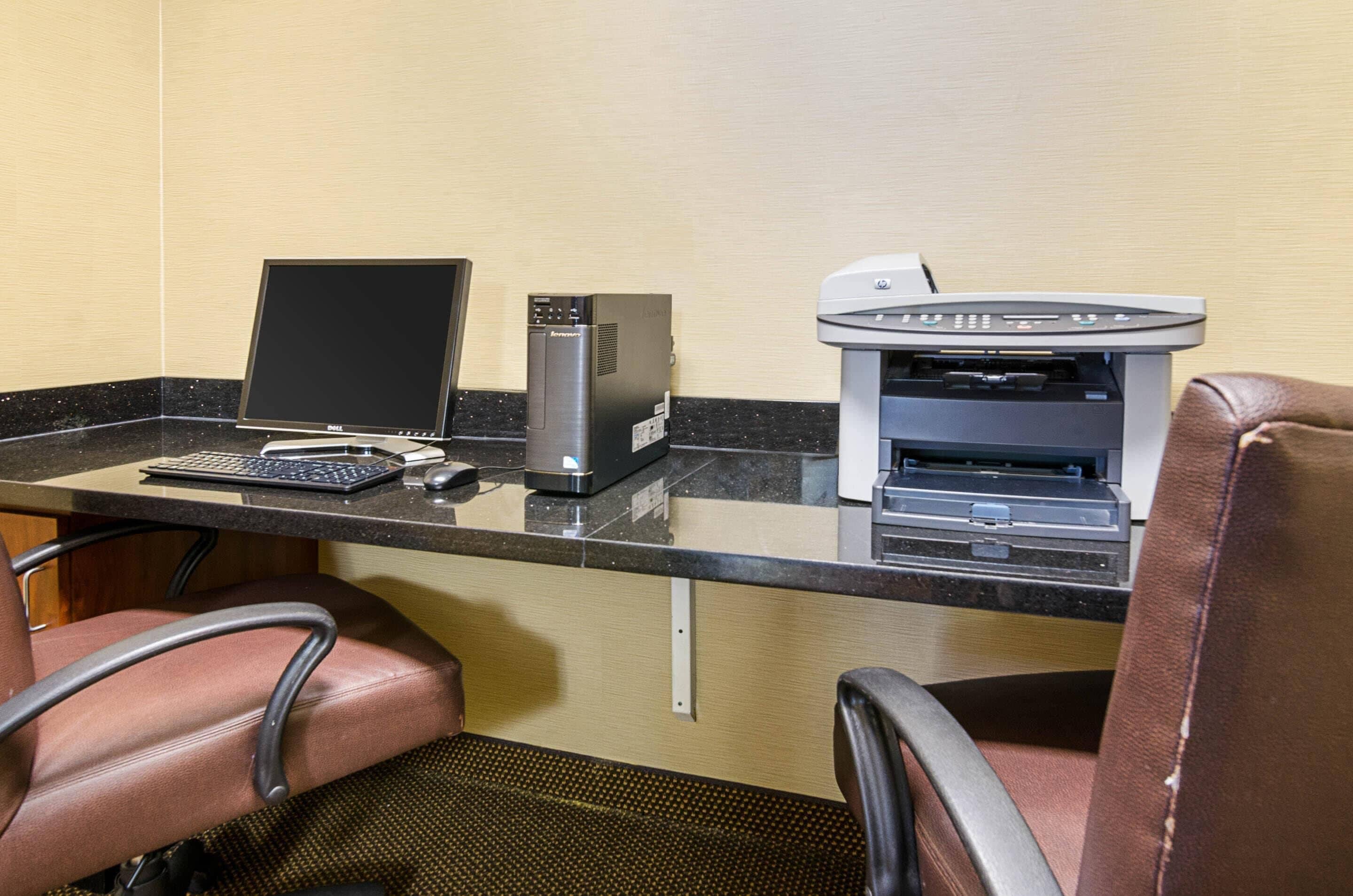 Un espacio de trabajo en un hotel con escritorio, computadora, impresora y dos sillones de cuero.