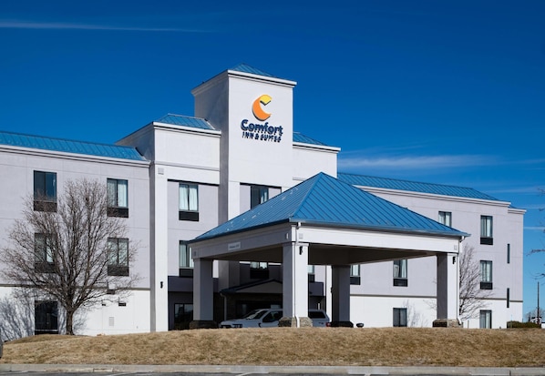 A modern Comfort Inn & Suites building with a covered parking area, a flat roof, and a clear blue sky.