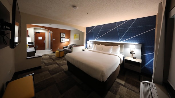 A hotel room with a large bed, a desk, a chair, a mirror, and a bathroom visible through an open door.