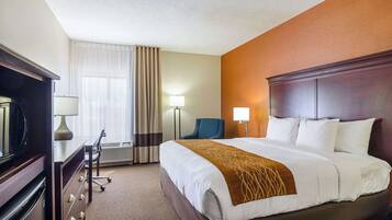 Ein Hotelzimmer mit einem großen Bett, einem Schreibtisch mit Lampe, einem Sessel und einem Fernseher.