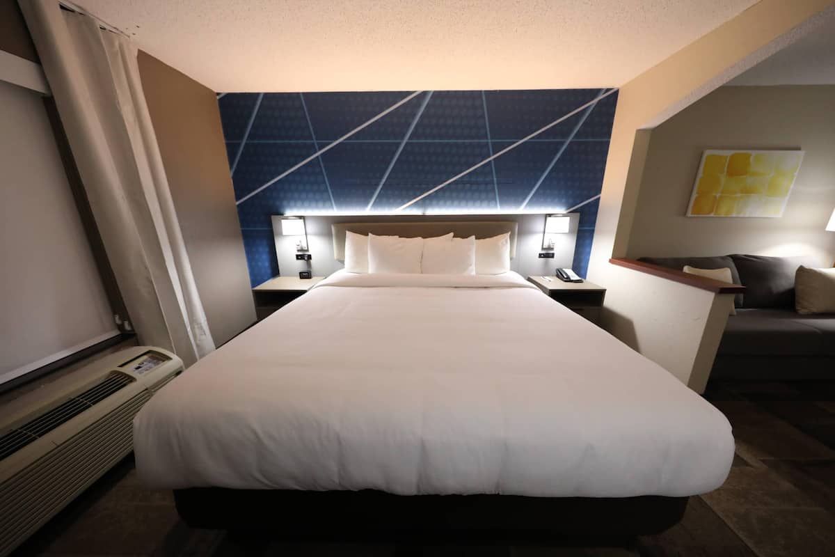 A hotel room with a large bed, a headboard with a geometric pattern, two bedside lamps, a small desk with a chair, and a couch.