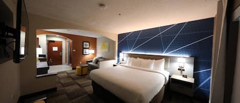 A hotel room with a large bed, a desk, a chair, a mirror, and a wall with geometric patterns.