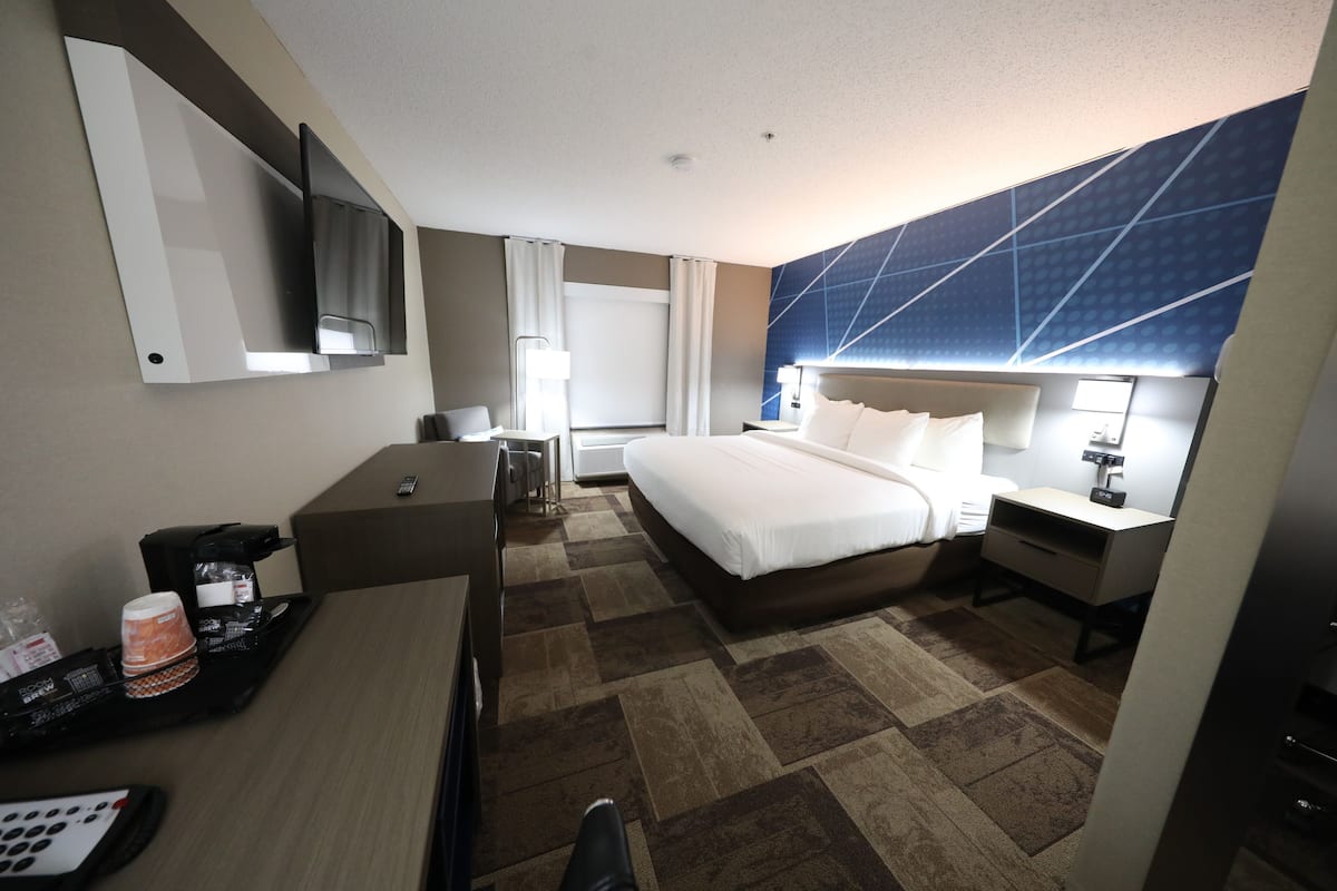 A hotel room with a bed, bedside table, desk, chair, and a TV mounted on the wall.