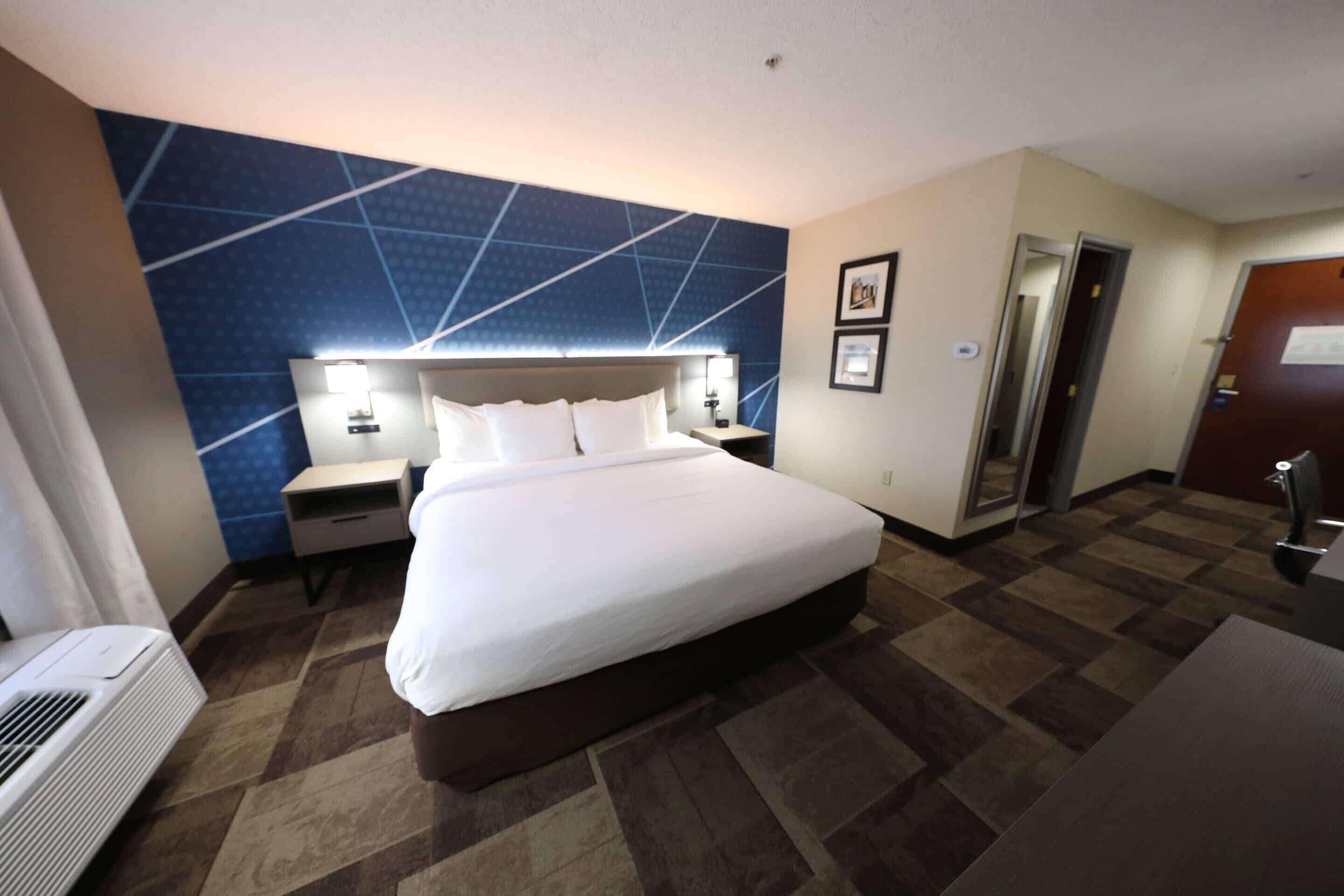 A hotel room with a large bed, a nightstand, a desk, a chair, a mirror, and a door.
