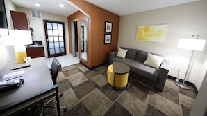 A hotel room with a conference table, a sofa, a small round table, and a lamp.