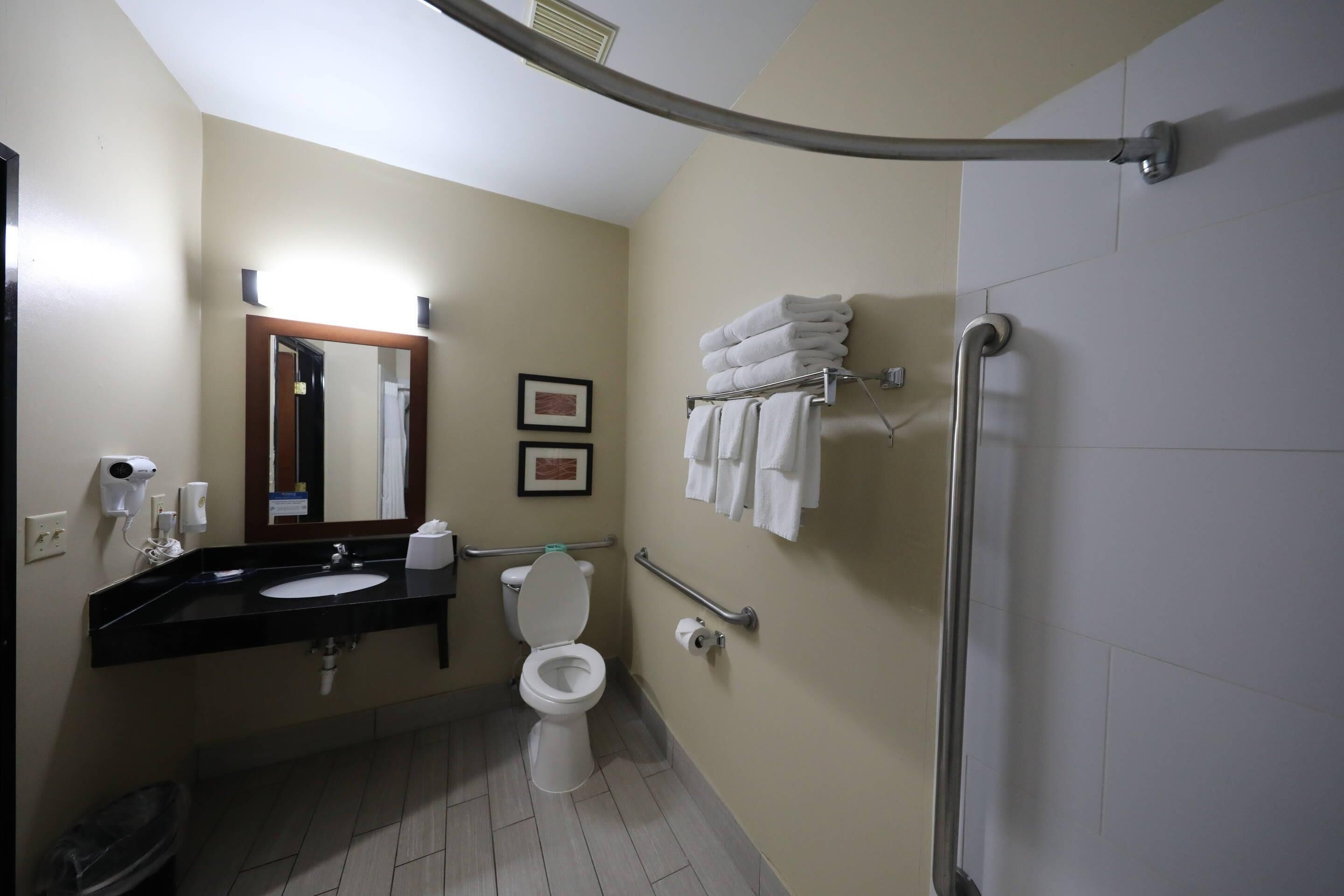 A bathroom with a toilet, sink, mirror, towel rack, and hand dryer.