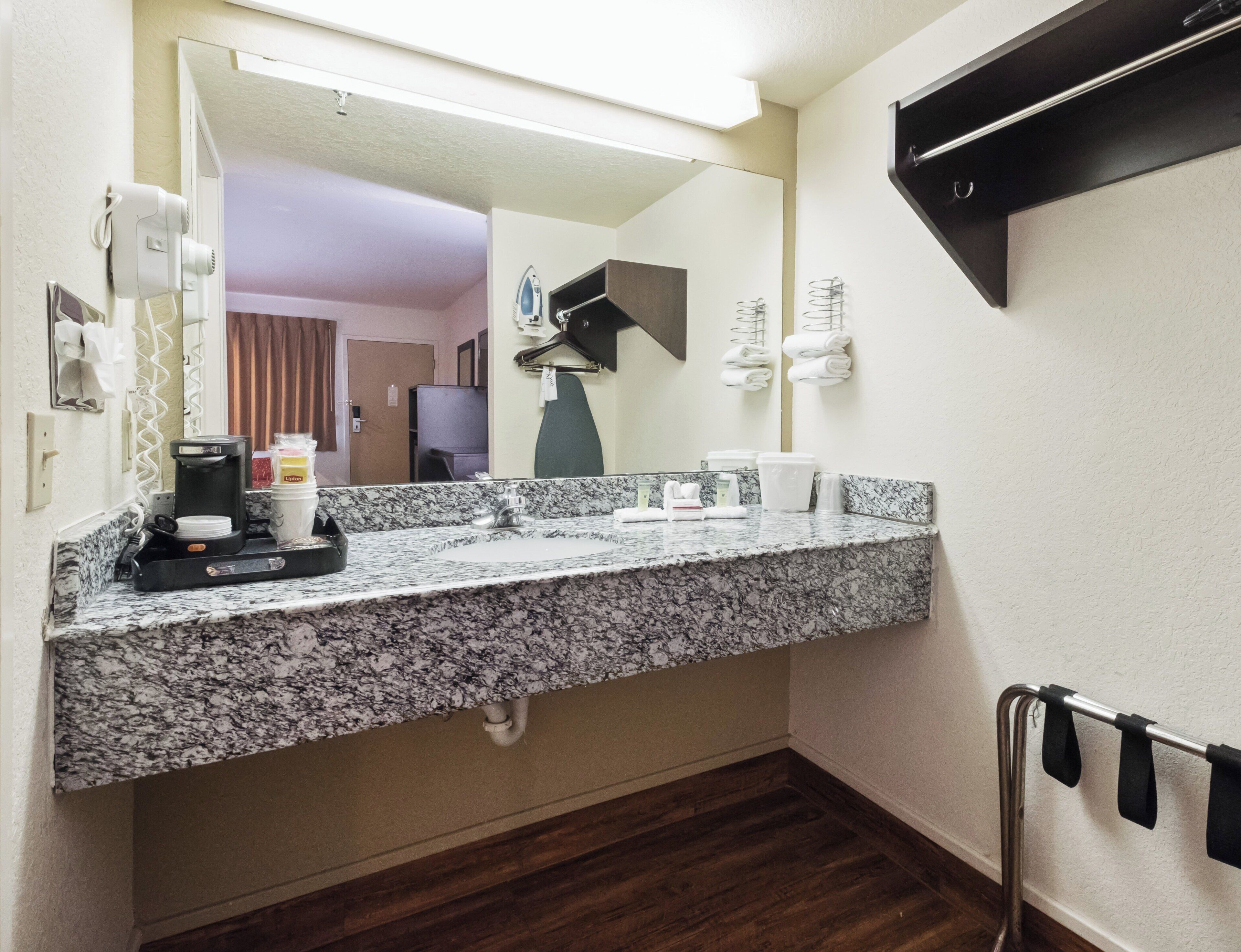 Een hotelbadkamer met een granieten aanrecht, een wastafel, een spiegel, een handdoekhouder en een koffiezetapparaat.