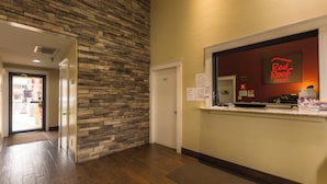 A hotel reception area with a stone wall, a reception desk, and a door leading to the hallway. - Red Roof Inn Oklahoma Airport – I-40 W/Fairgrounds (Oklahoma City)