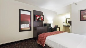 A hotel room with a bed, a desk, a chair, a TV mounted on the wall, a mirror, and a patterned carpet. - Red Roof Inn Oklahoma Airport – I-40 W/Fairgrounds (Oklahoma City)
