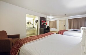 A hotel room with two beds, a TV, a desk, and a bathroom visible through an open door.