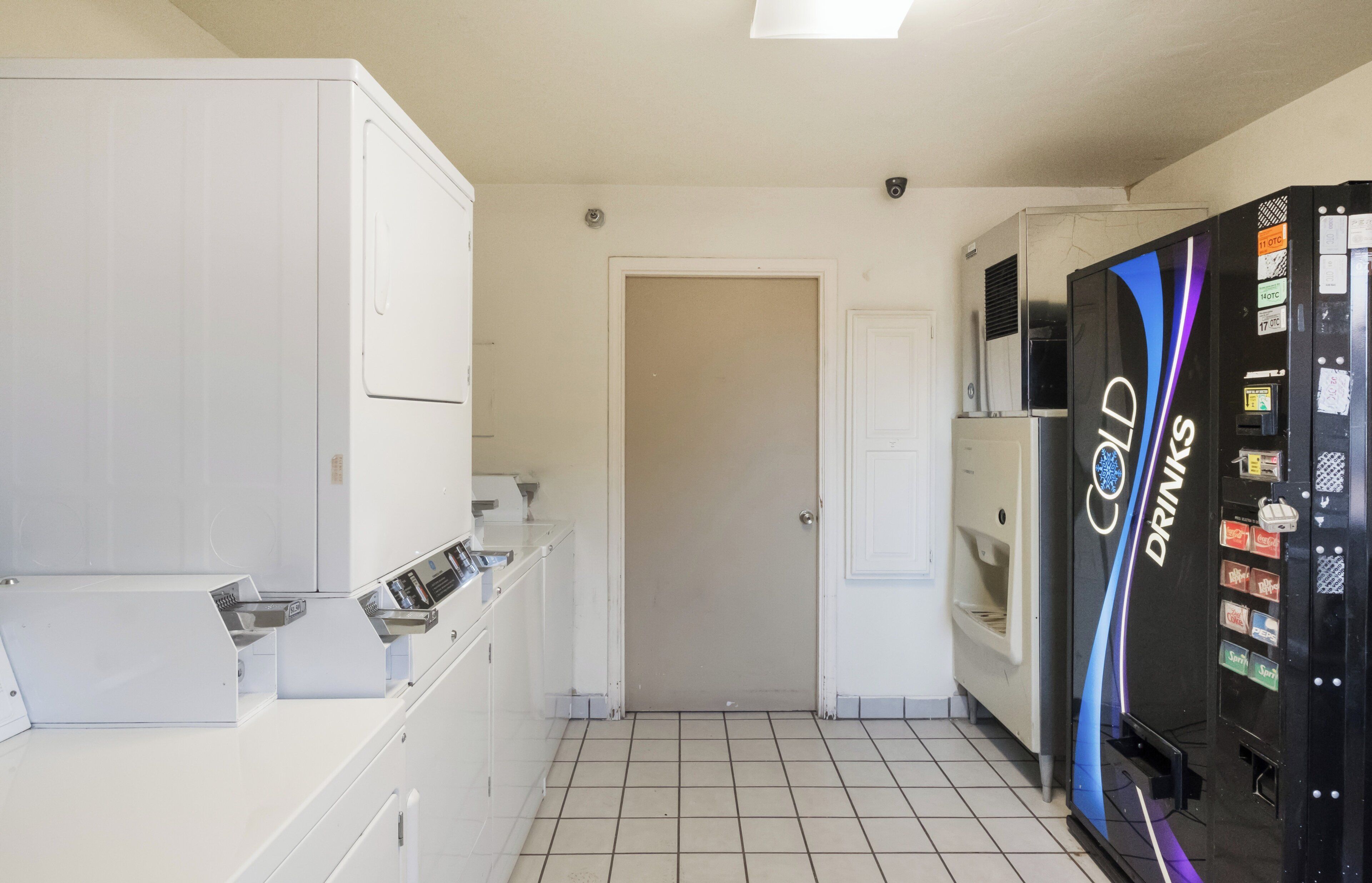 A hotel room with a white wardrobe, a door, a tiled floor, and a vending machine with drink options.