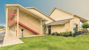 A motel with a covered walkway, a small tree, and a recycling bin. - Red Roof Inn Oklahoma Airport – I-40 W/Fairgrounds (Oklahoma City)