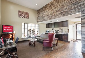 A spacious living area with a stone accent wall, a large window, and a kitchen in the background. - Red Roof Inn Oklahoma Airport – I-40 W/Fairgrounds (Oklahoma City)