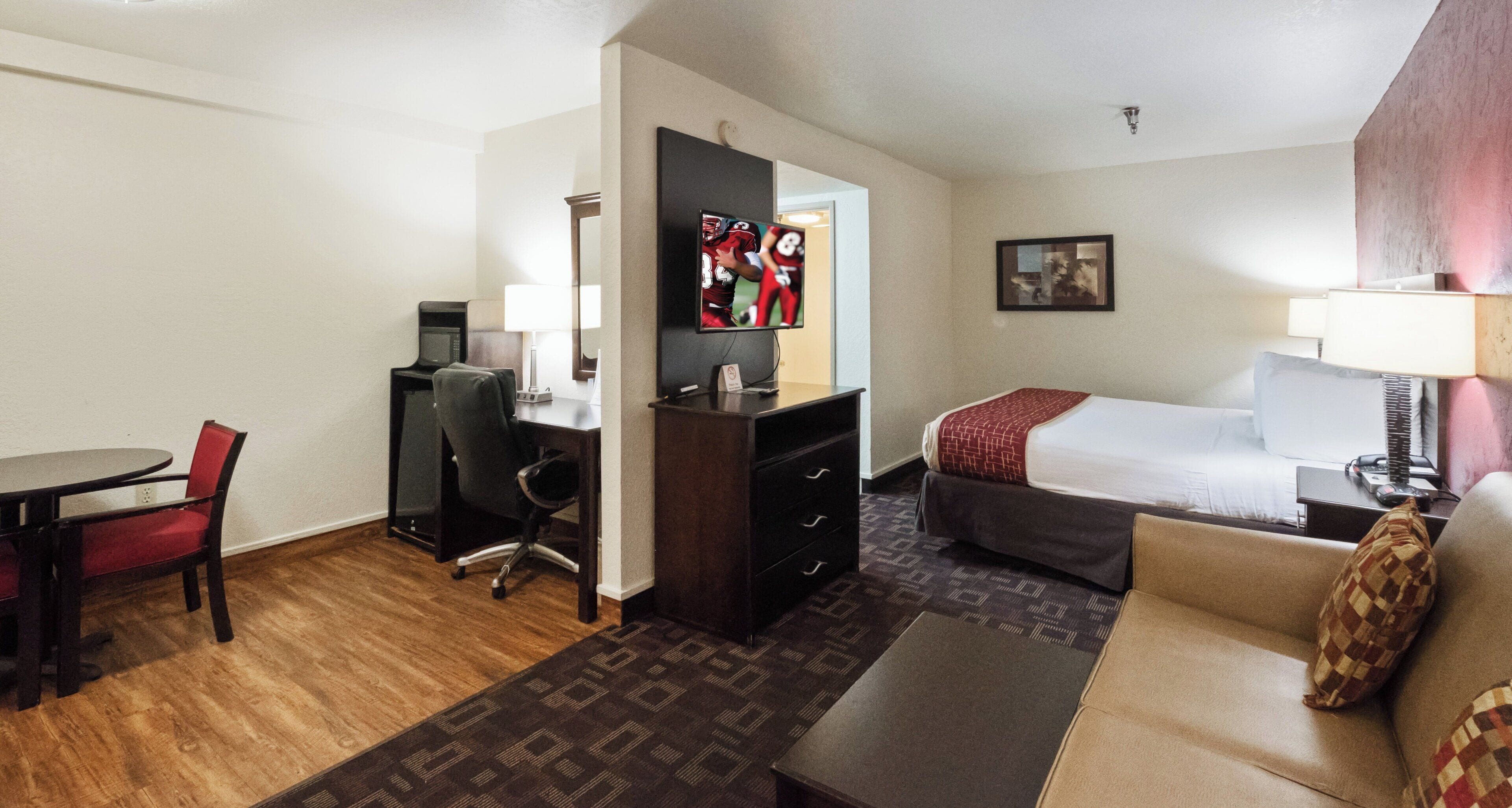 Een hotelkamer met een bureau, stoel, bed en een aan de muur bevestigde televisie.