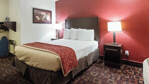 A hotel room with a large bed, a nightstand with a lamp, a wall-mounted TV, and a red accent wall. - Red Roof Inn Oklahoma Airport – I-40 W/Fairgrounds (Oklahoma City)