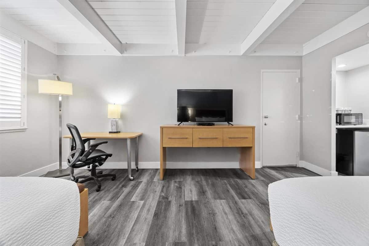 A hotel room with a wooden desk, a television, a chair, and a bed.