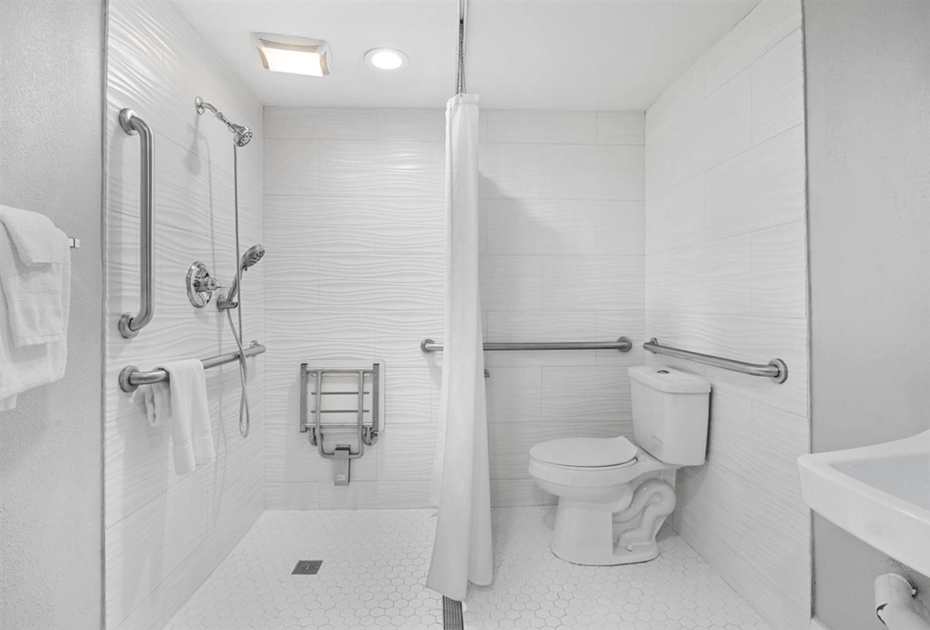 Une salle de bain moderne équipée d’une douche, de toilettes et d’un lavabo. Elle comprend également des barres d’appui et un porte-serviettes.