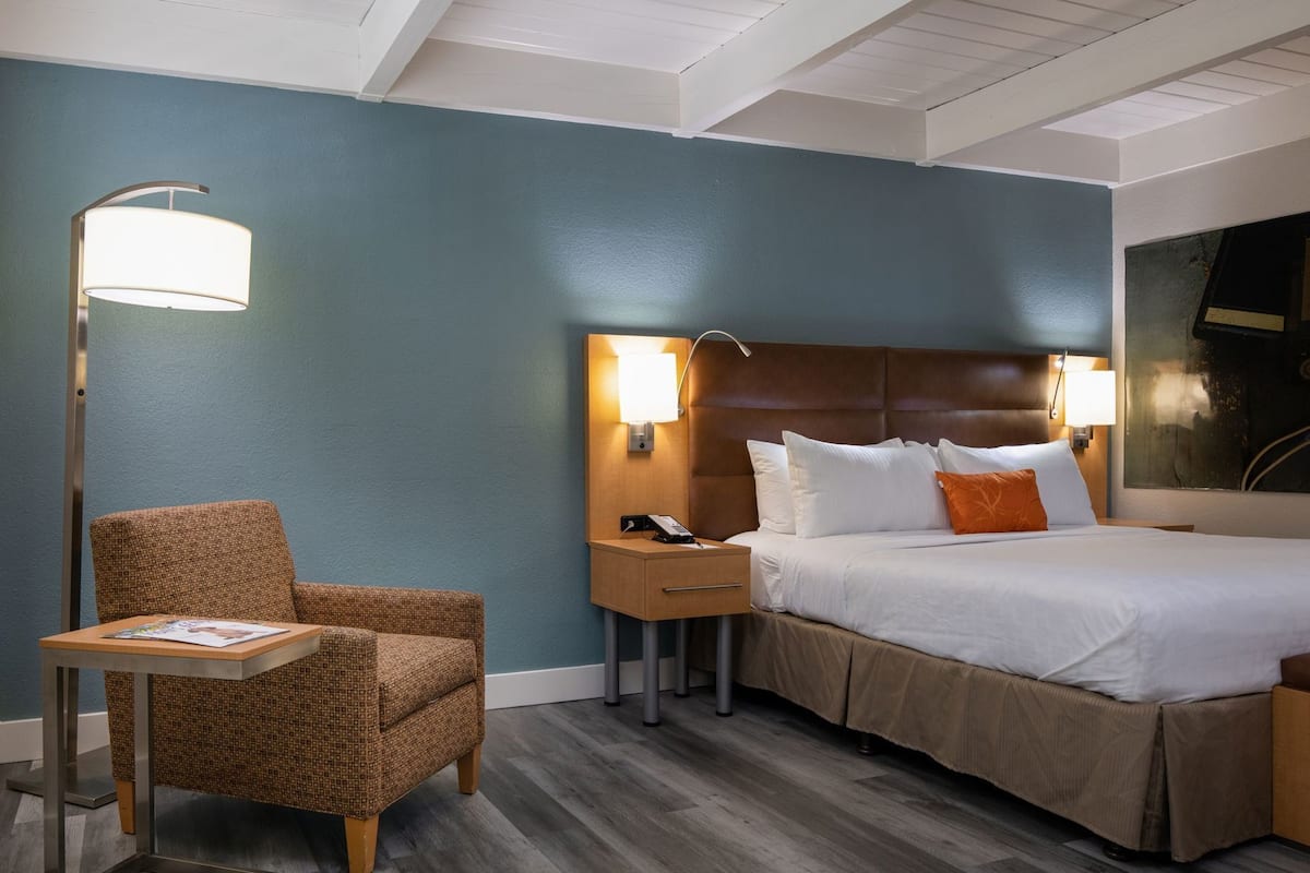 A hotel room with a bed, a nightstand, a lamp, a chair, and a table.