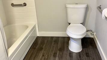 Une salle de bain avec des toilettes blanches, une baignoire et un plancher en bois.