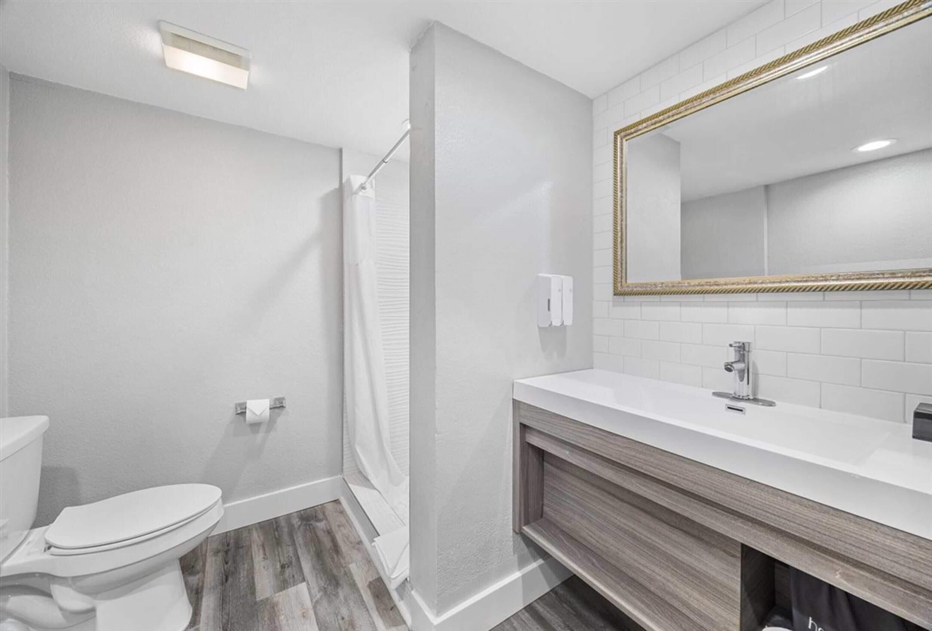 Et moderne badeværelse med toilet, bruser og vaskebord med spejl.
