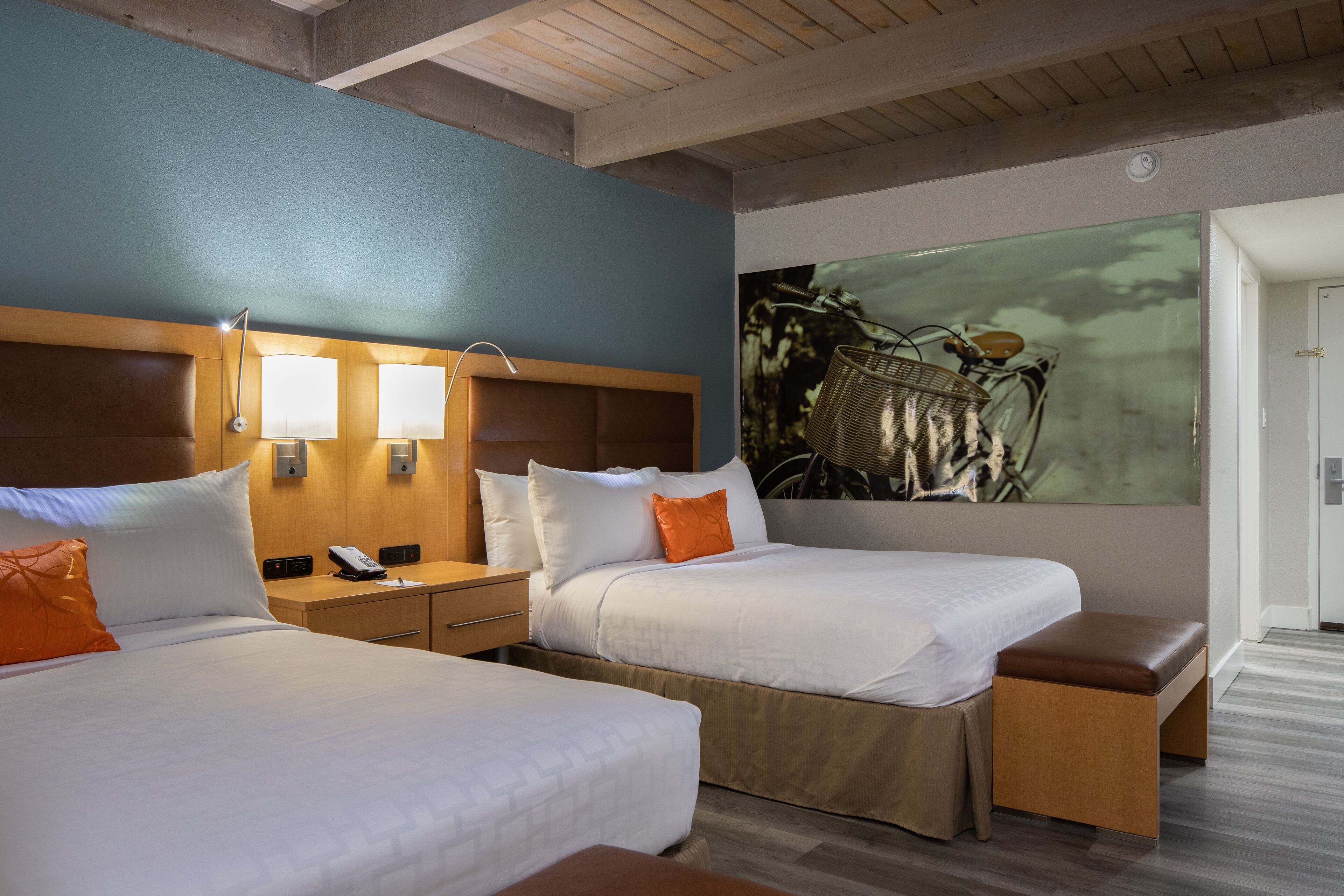 A hotel room with two beds, a wooden headboard, a nightstand with a phone, and a large abstract painting on the wall.