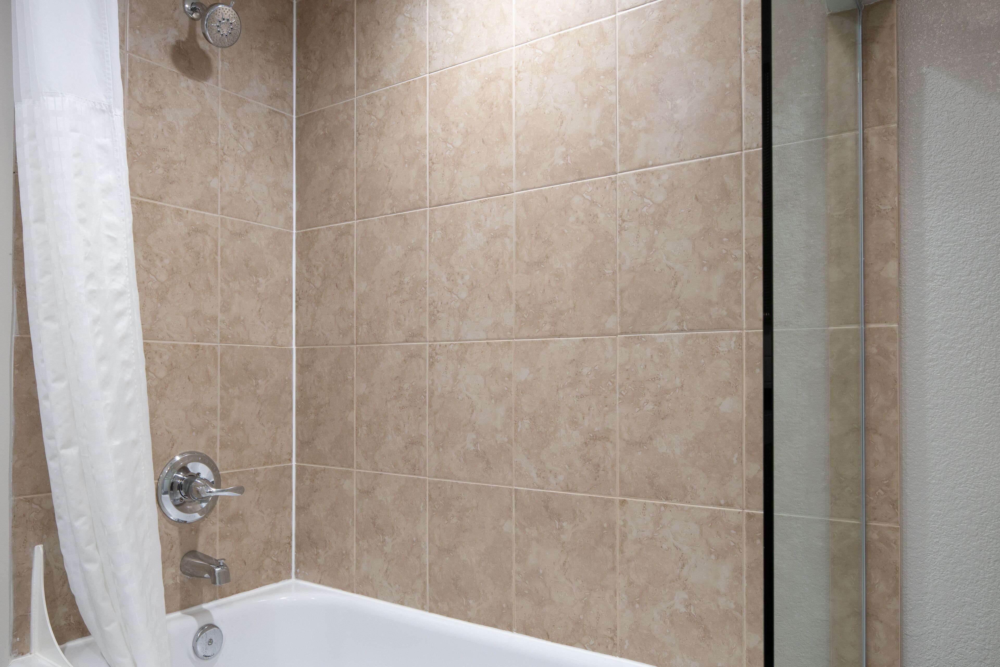 Un baño moderno con baldosas color beige, una bañera y una ducha con puerta de cristal.