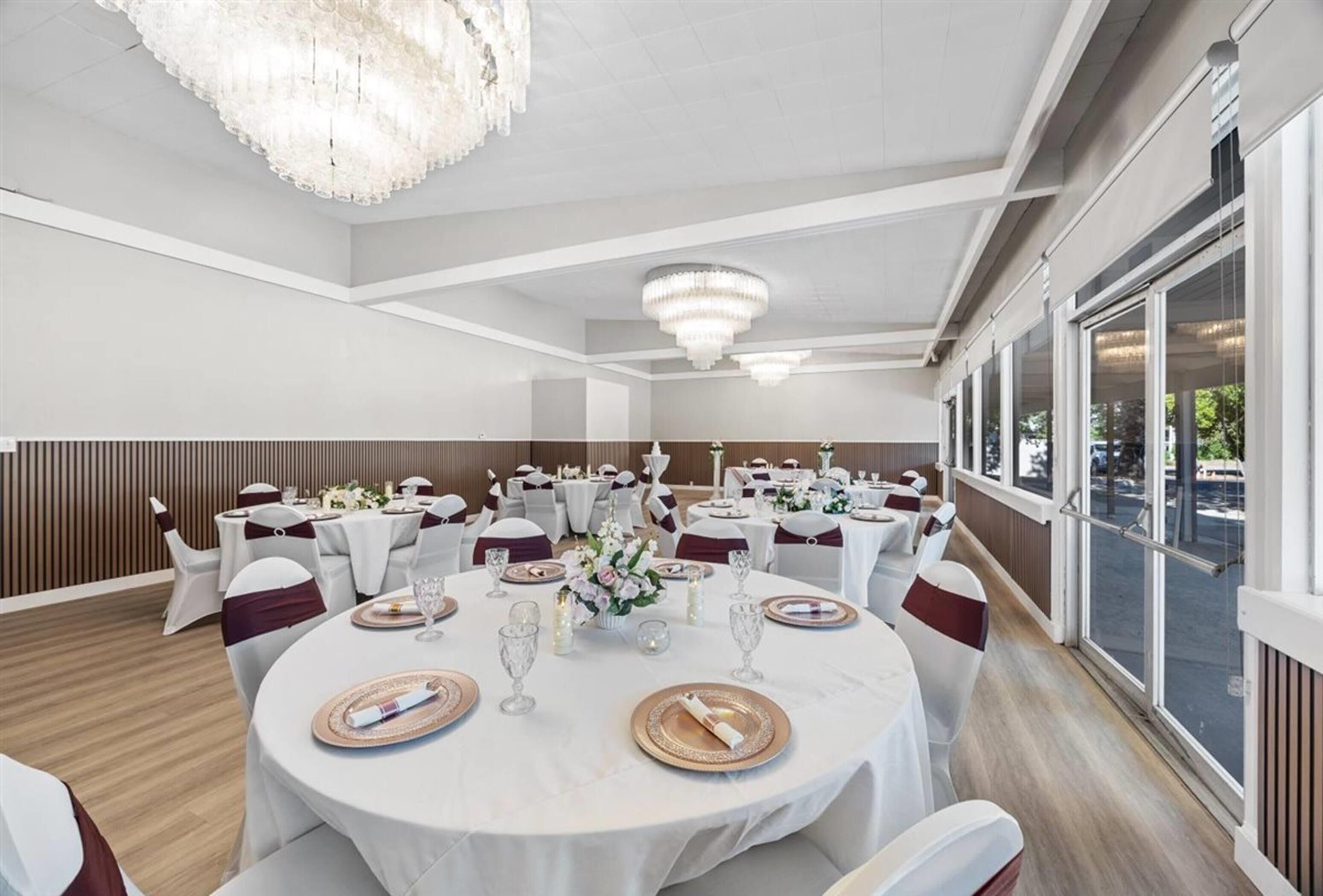 Un salón de banquetes con mesas redondas dispuestas para un evento formal, con candelabros y ventanas amplias.