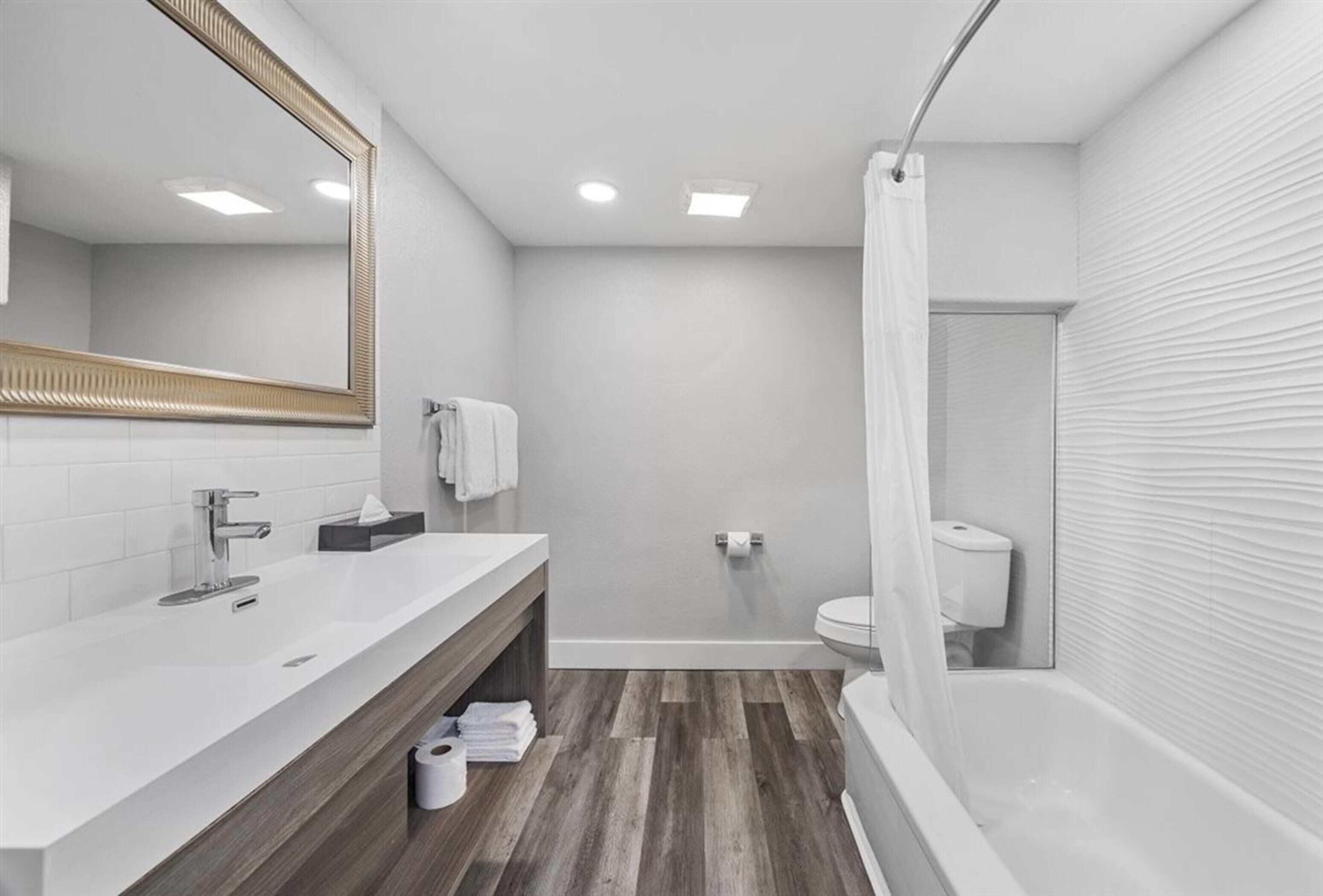 Une salle de bain moderne avec un grand miroir, un lavabo blanc, un meuble-lavabo en bois et une baignoire.